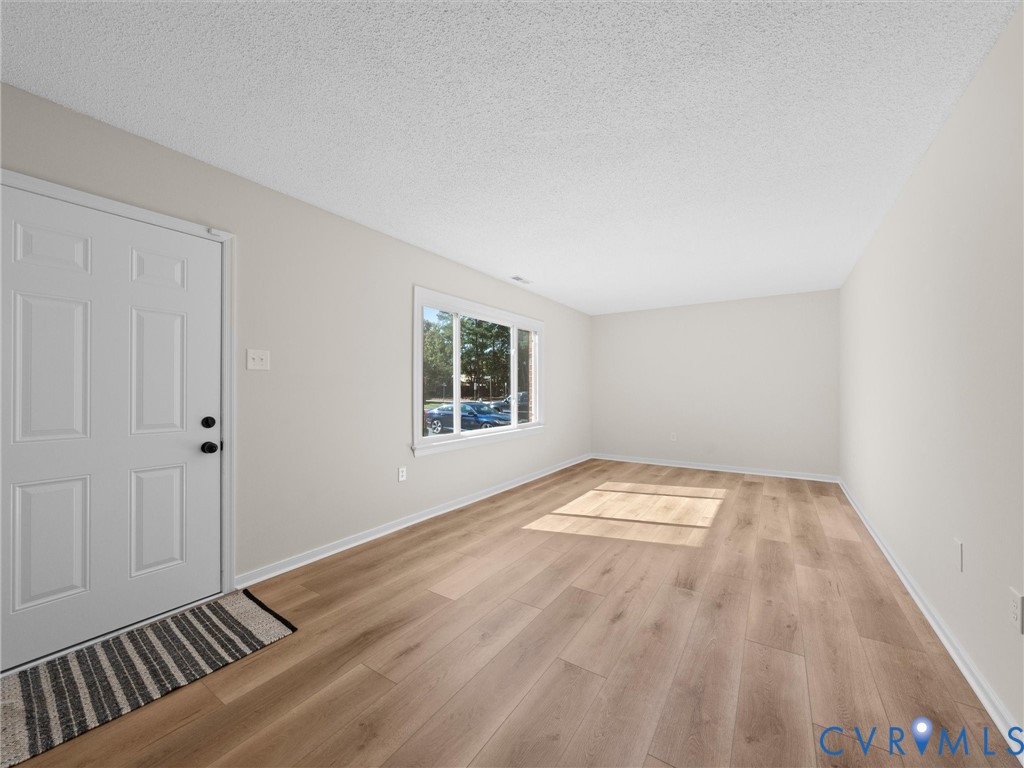 Neutral-toned interior space featuring light wood-finish flooring, a six-panel exterior entry door, and a large single-pane window with white trim