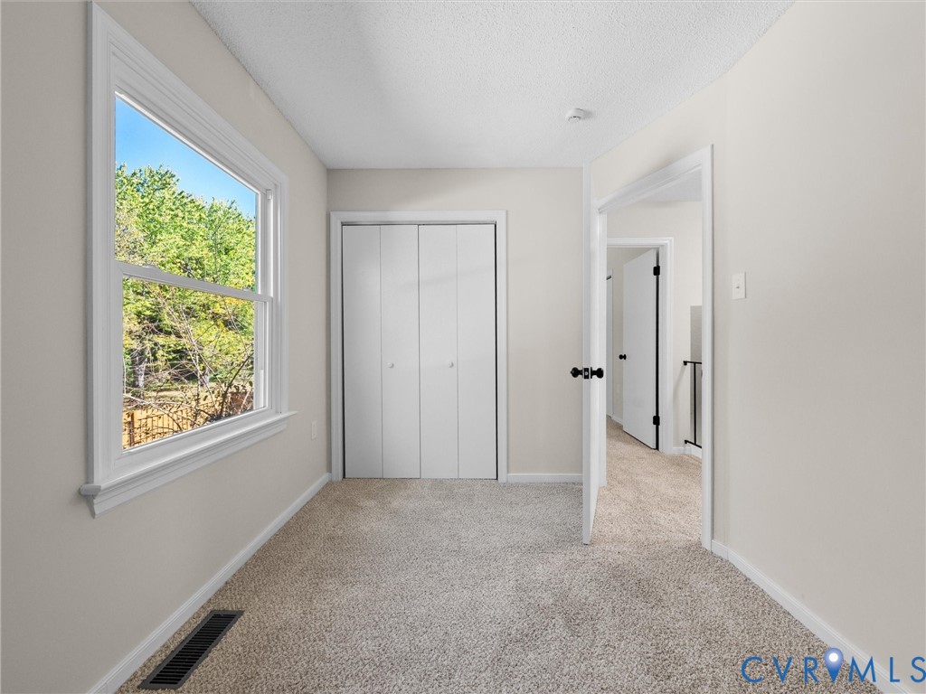Neutral-toned interior space featuring neutral wall-to-wall carpeting, a single-hung window with white trim, and a double-door closet with white folding panels