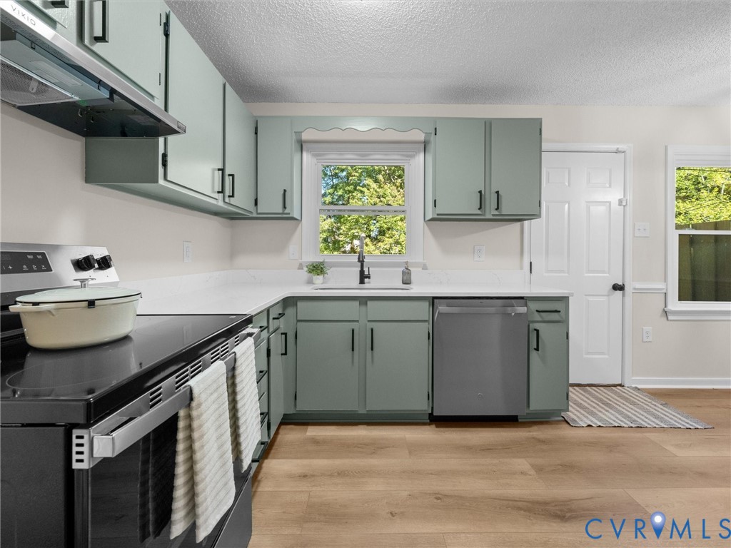 Kitchen featuring light-toned cabinetry with dark hardware, solid-surface countertops, wood-finish flooring, and stainless steel appliances