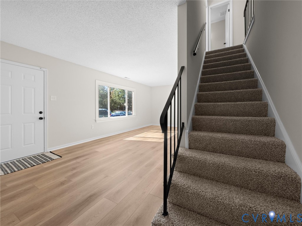 Entryway featuring wood-finish flooring, a multi-pane window, and a staircase with carpeted treads and a metal handrail