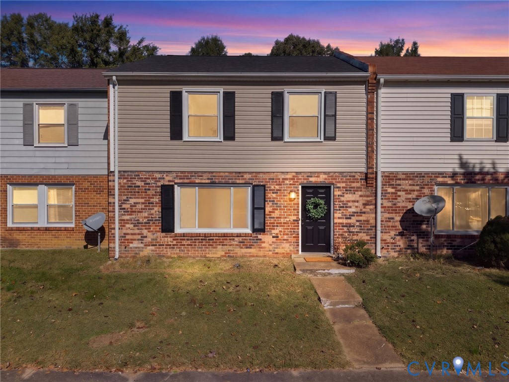 Two-story townhouse exterior featuring a multi-material facade of brick and vinyl siding, shutters on all windows, and a concrete front walkway