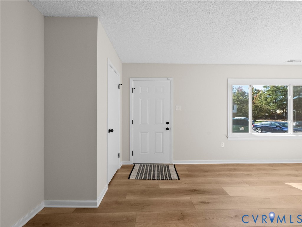 Neutral-toned interior featuring wood-finish flooring, a six-panel entry door, and an expansive picture window