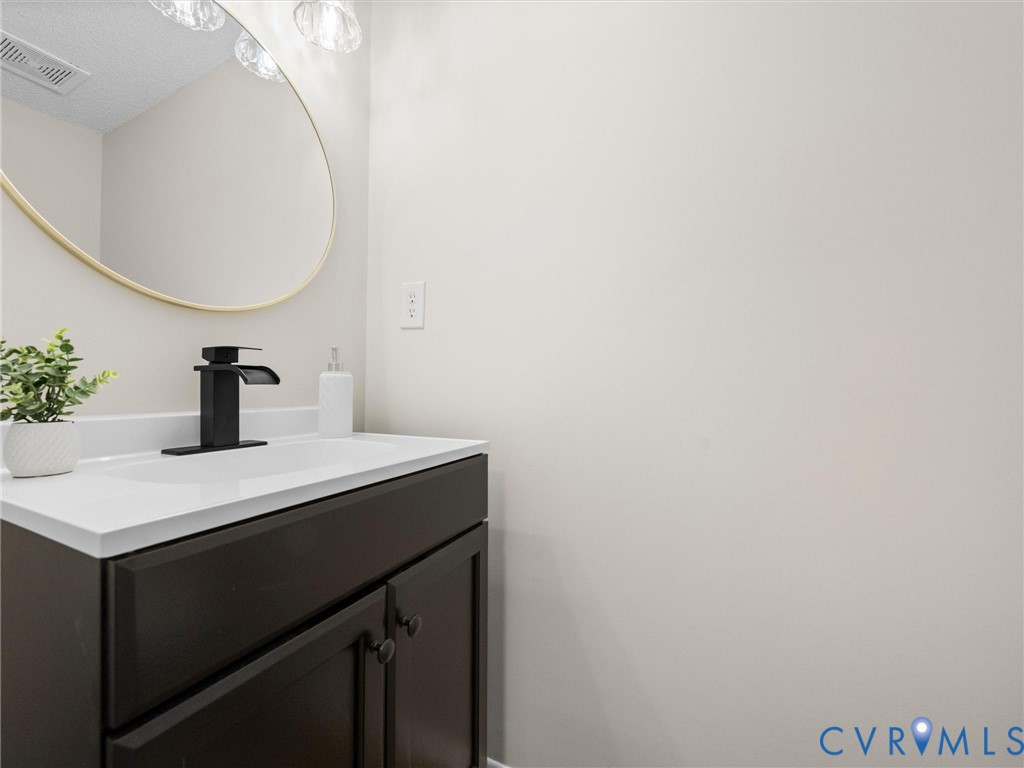 Dark cabinetry vanity with a white countertop, integrated sink, matte black faucet, and an oval mirror with a gold-finish frame