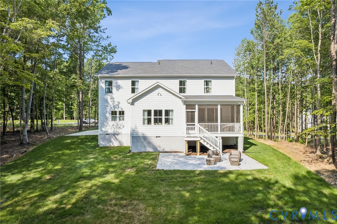 Two-story exterior with white siding, screened-in porch, staircase, concrete patio, and mature tree-lined perimeter Two-story exterior with white siding, screened-in porch, staircase, concrete patio, and mature tree-lined perimeter