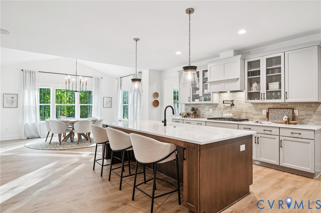 Kitchen featuring a center island with a stone-finish countertop, shaker-style cabinetry, recessed lighting, pendant fixtures, and wood-finish flooring