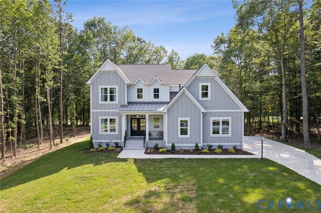 Two-story residence featuring light gray vertical siding, a metal roof accent over the entryway, multi-pane windows, and a paved driveway