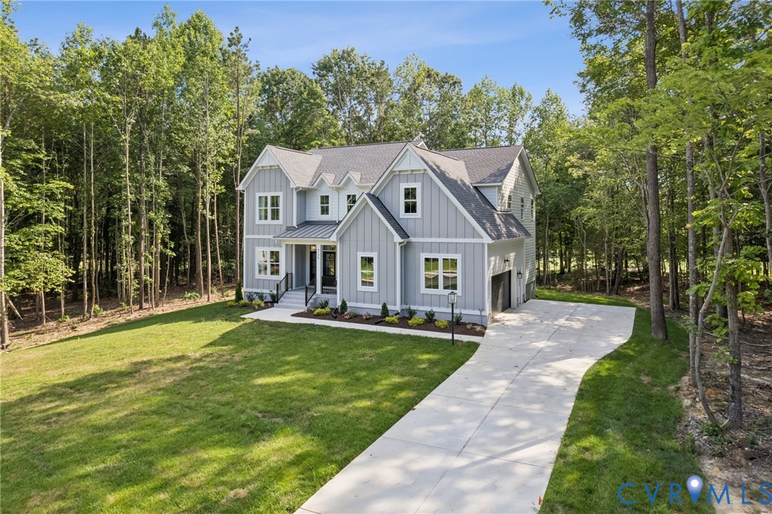 Two-story residence featuring vertical siding, a metal accent roof over the entry, a shingled roof, a concrete driveway, and a natural wooded backdrop