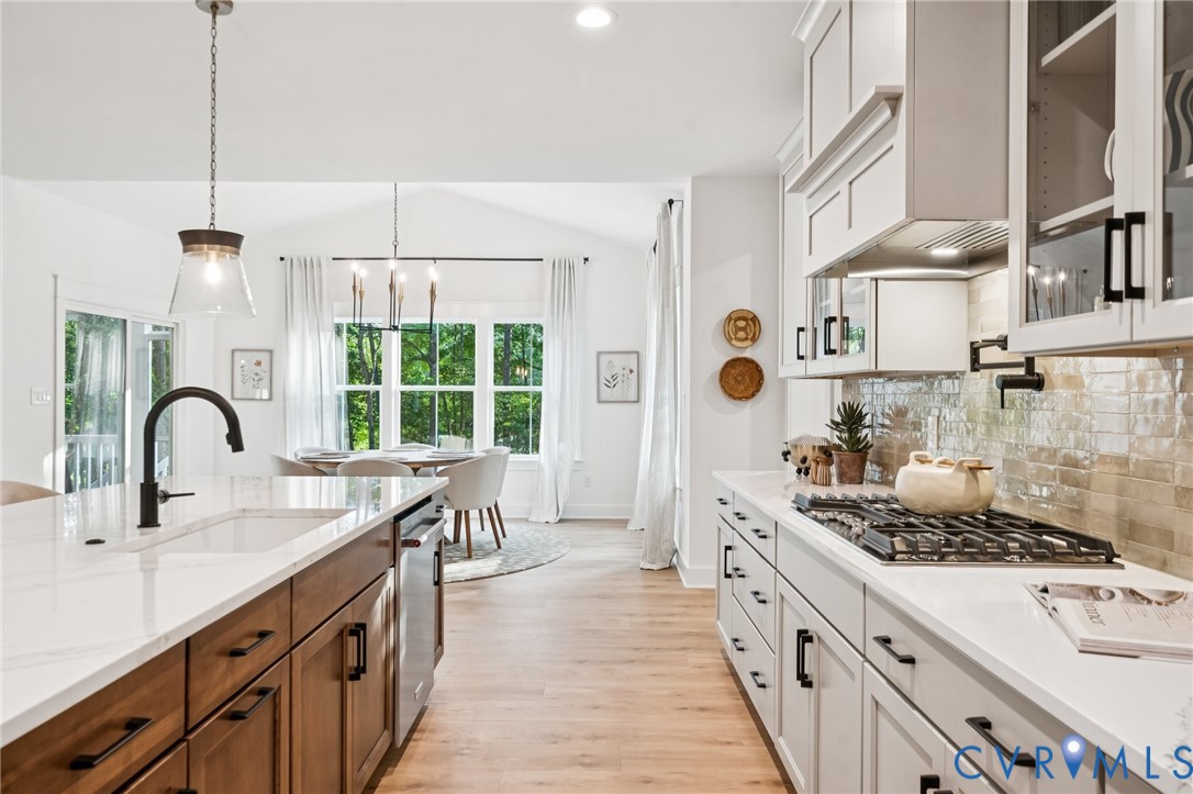 Kitchen featuring white and wood-finish cabinetry, stone-style countertops, a tile backsplash, gas range with pot filler, and wood-finish flooring