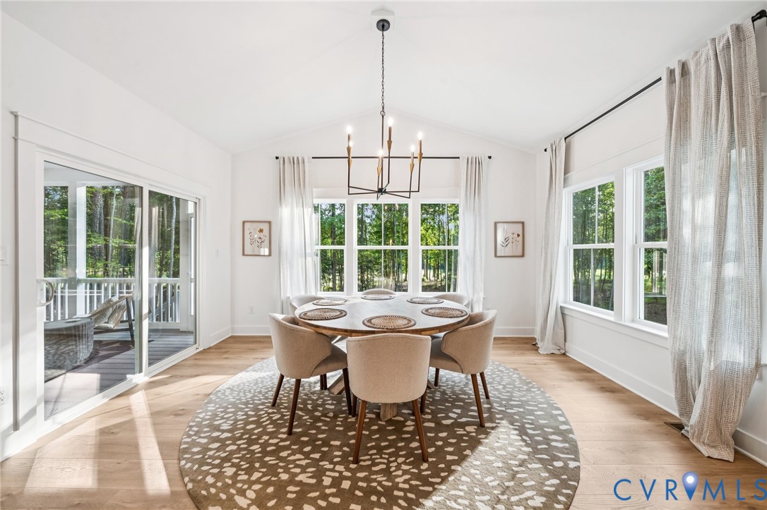 Vaulted ceilings, wood-finish flooring, multi-pane windows, a linear metal chandelier, and a sliding glass door
