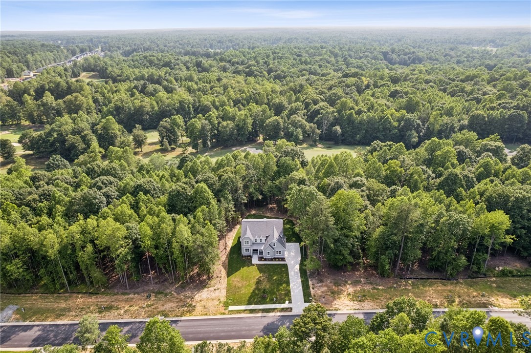Aerial perspective of a detached residence featuring a pitched roof, light-toned siding, a concrete driveway, and expansive wooded surroundings Aerial perspective of a detached residence featuring a pitched roof, light-toned siding, a concrete driveway, and expansive wooded surroundings