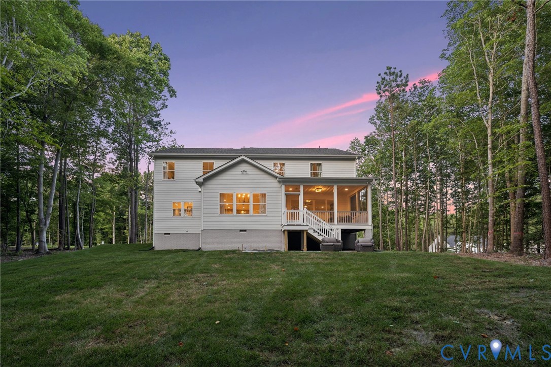Two-story residence featuring light-colored horizontal siding, a raised rear screened porch with white railing, and an expansive lawn bordered by mature trees Two-story residence featuring light-colored horizontal siding, a raised rear screened porch with white railing, and an expansive lawn bordered by mature trees
