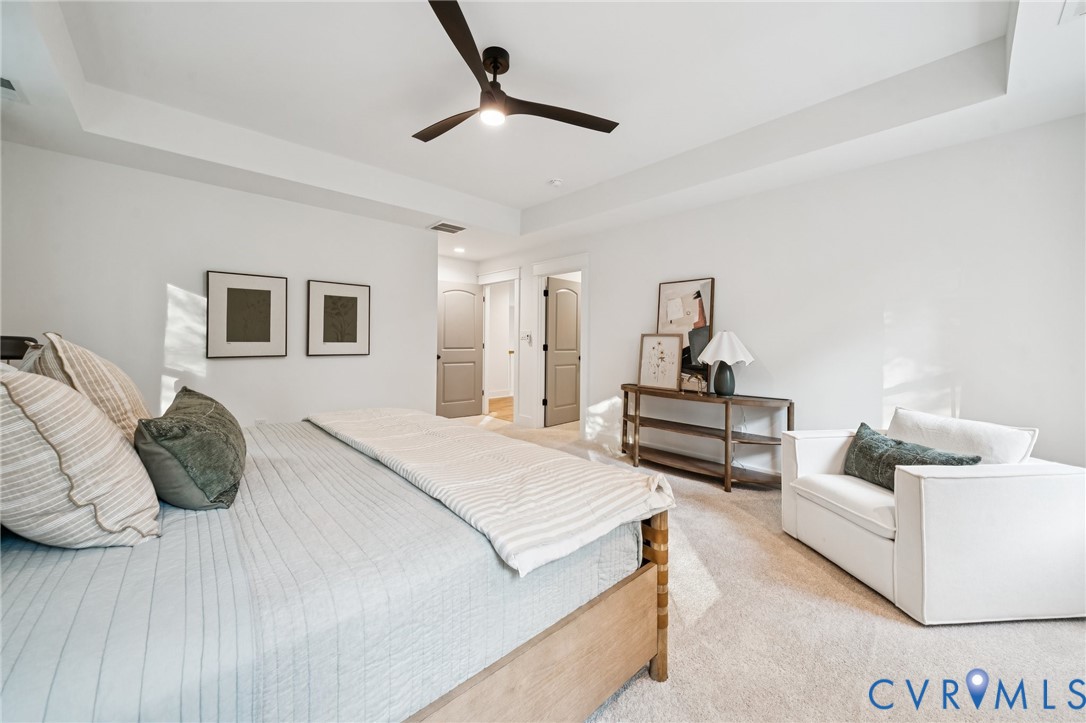 Tray ceiling featuring a contemporary matte black ceiling fan with integrated lighting, neutral carpeting, and two-panel arch-top interior doors