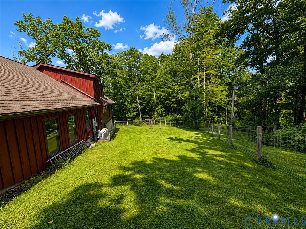 Expansive backyard featuring a manicured lawn, perimeter wire fencing, and a red vertical-board siding exterior