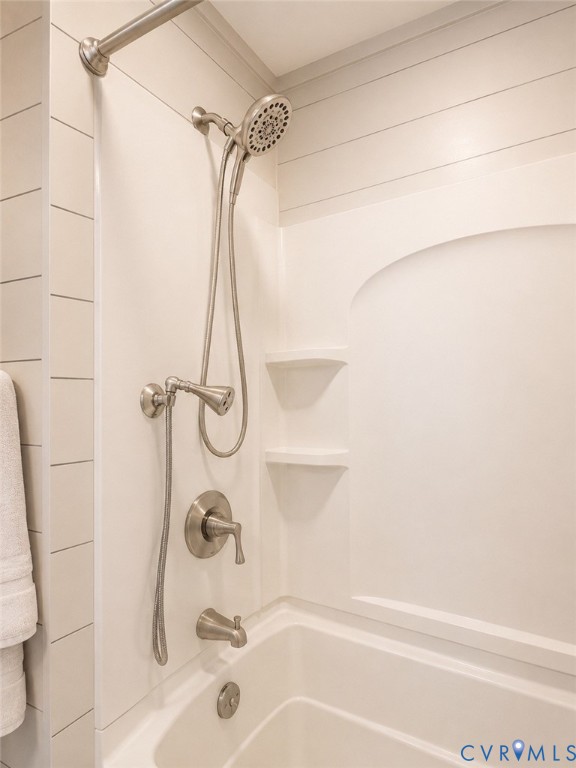 Shower and tub combination featuring brushed nickel finish hardware, integrated shelving, an adjustable handheld shower head, and horizontally paneled wall detailing