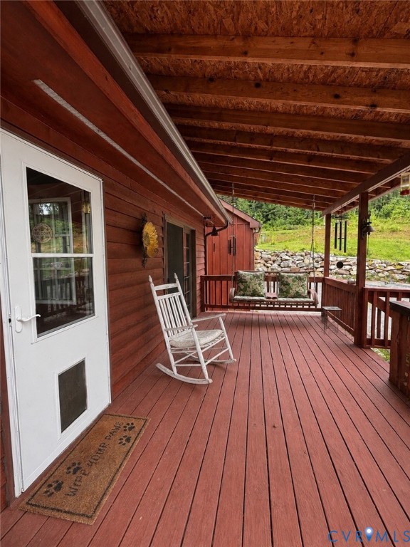 Covered wooden deck featuring exposed rafters, horizontal wood siding, and a wooden railing