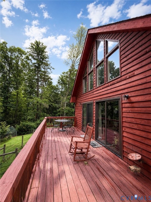 Red wood-sided exterior featuring an expansive wrap-around deck, floor-to-ceiling glass sliding doors, and large triangular windows