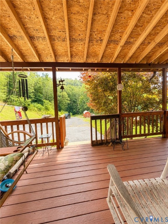 Covered wooden porch featuring exposed timber rafters, stained wood decking, and a perimeter railing