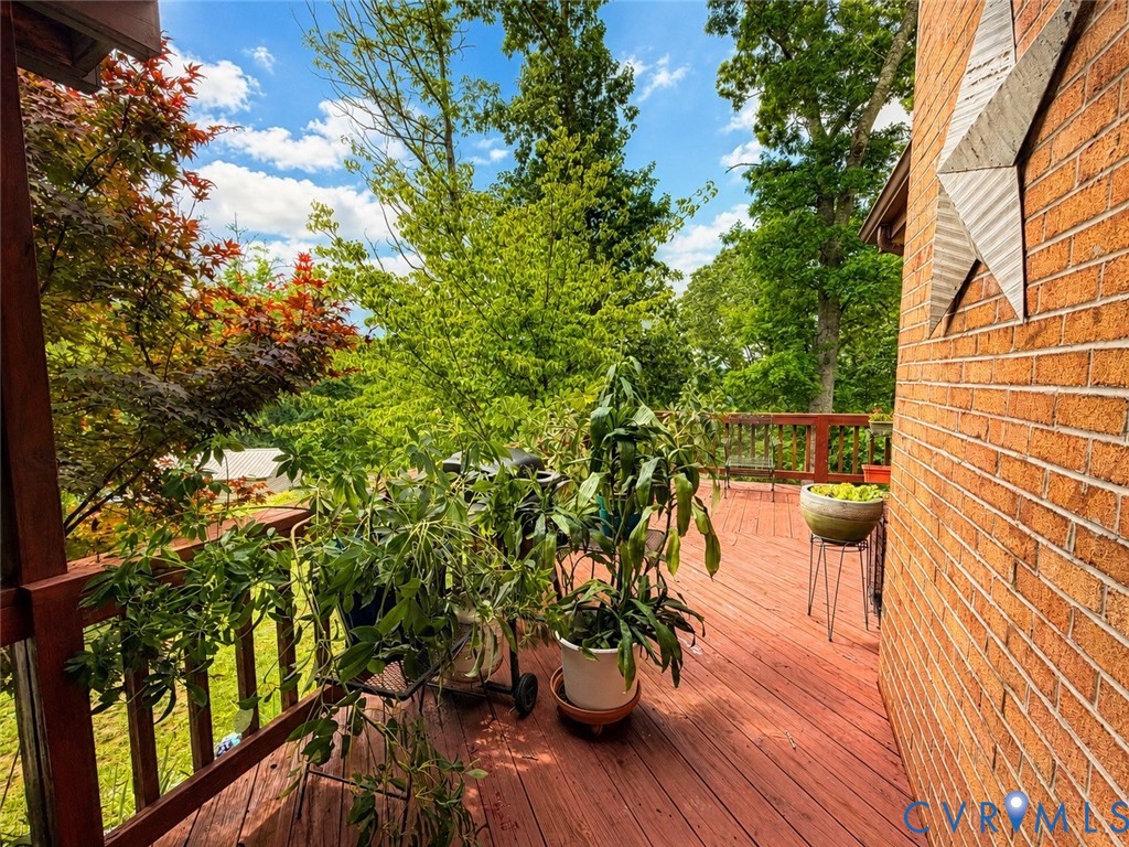Spacious outdoor deck with wood-finish decking, anchored by a brick exterior wall and surrounding mature trees