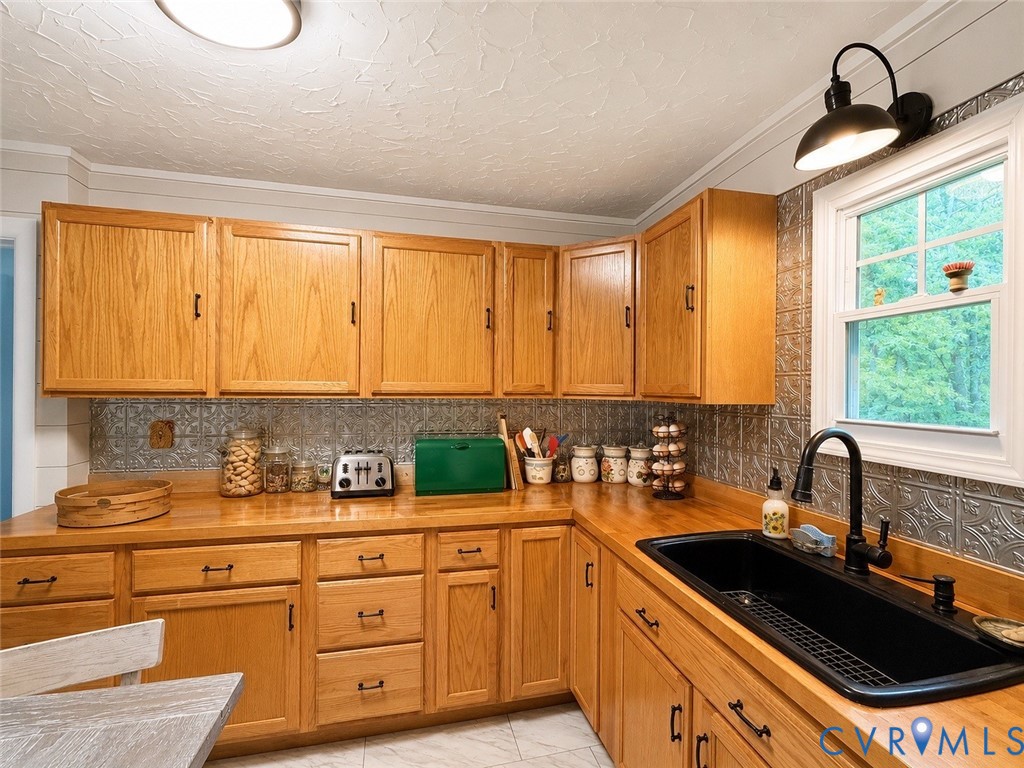Kitchen featuring natural wood cabinetry, wood countertops, metal tile backsplash, matte black farmhouse sink, and a gooseneck faucet