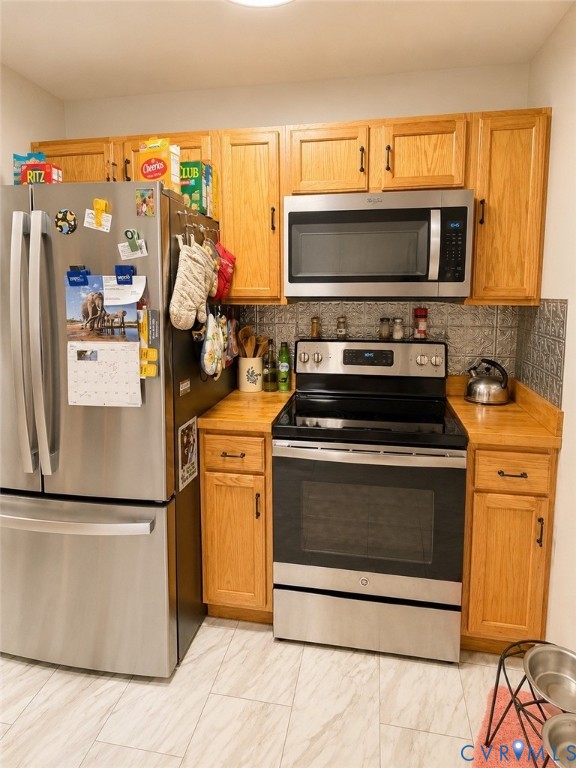 Kitchen featuring oak cabinetry, stainless steel appliances, a built-in microwave, stone-patterned tile backsplash, and tile flooring