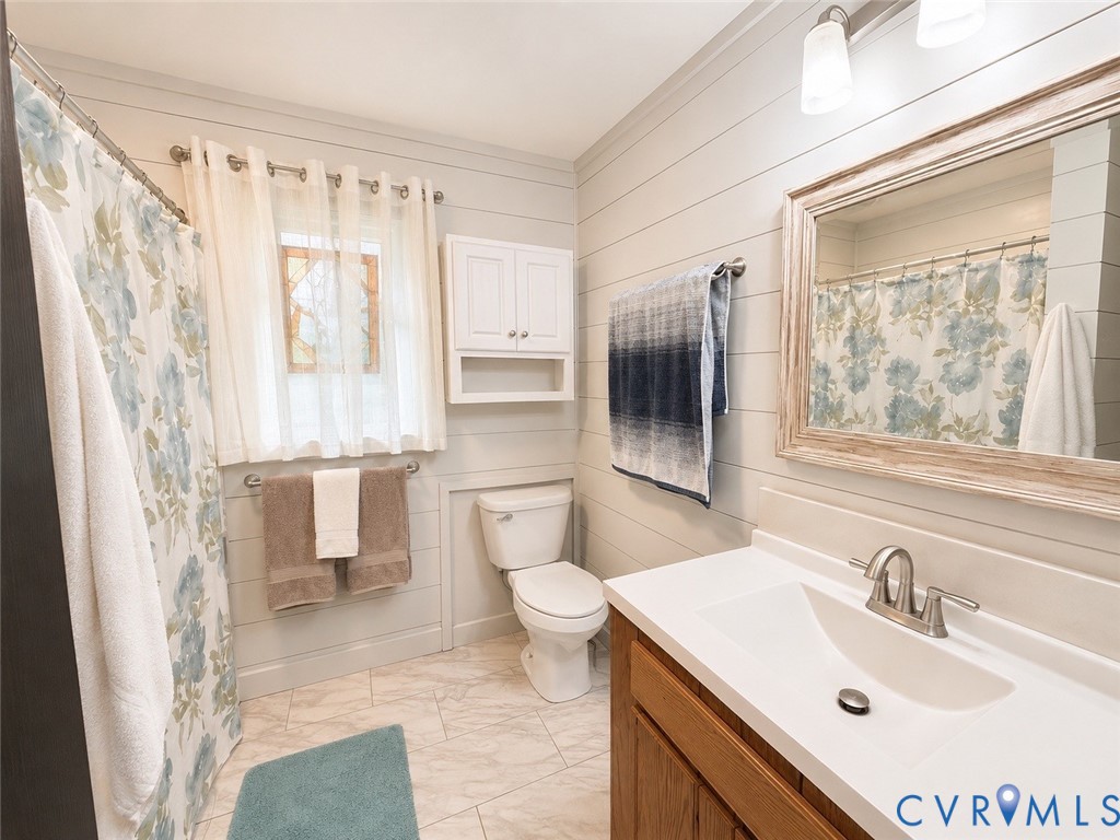 Bathroom featuring horizontal shiplap wall paneling, vanity with an integrated countertop and basin, wall-mounted cabinetry, polished metal faucet, and multi-tone tiled flooring