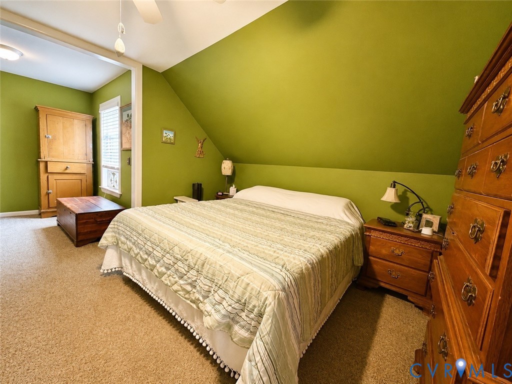 Bedroom featuring a vaulted ceiling with a sloped wall, wall-to-wall carpeting, and a multi-pane window