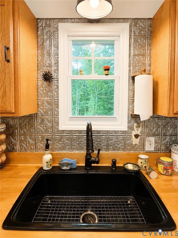 Metallic patterned tile backsplash, wood-finish countertops, black composite undermount sink, high-arc faucet, and single-hung window with wood-finish cabinetry