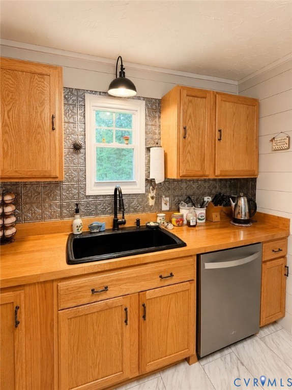 Kitchen featuring wood cabinetry, solid wood countertops, black composite basin sink with a matte black pull-down faucet, patterned metal tile backsplash, and stainless steel dishwasher