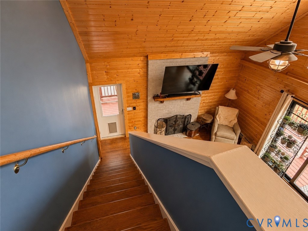 Vaulted ceiling with wood-plank paneling, brick fireplace featuring a wood mantel, and wood-finish flooring