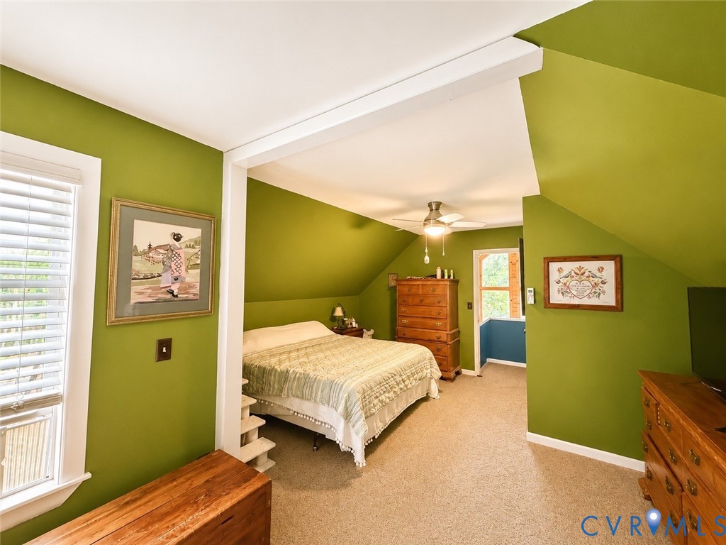 Sloped ceilings with an exposed structural support beam, carpeted flooring, and a ceiling fan with integrated lighting