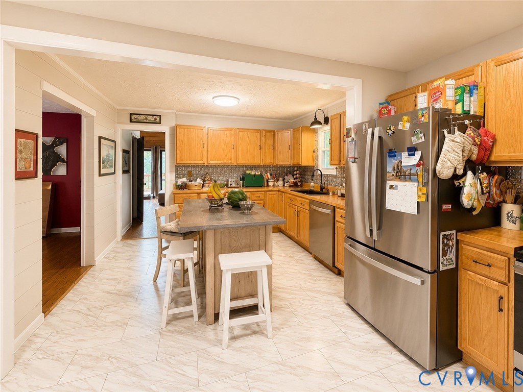 Kitchen featuring wood cabinetry, stainless steel appliances, central island with a rectangular countertop, patterned tile flooring, and a tiled backsplash