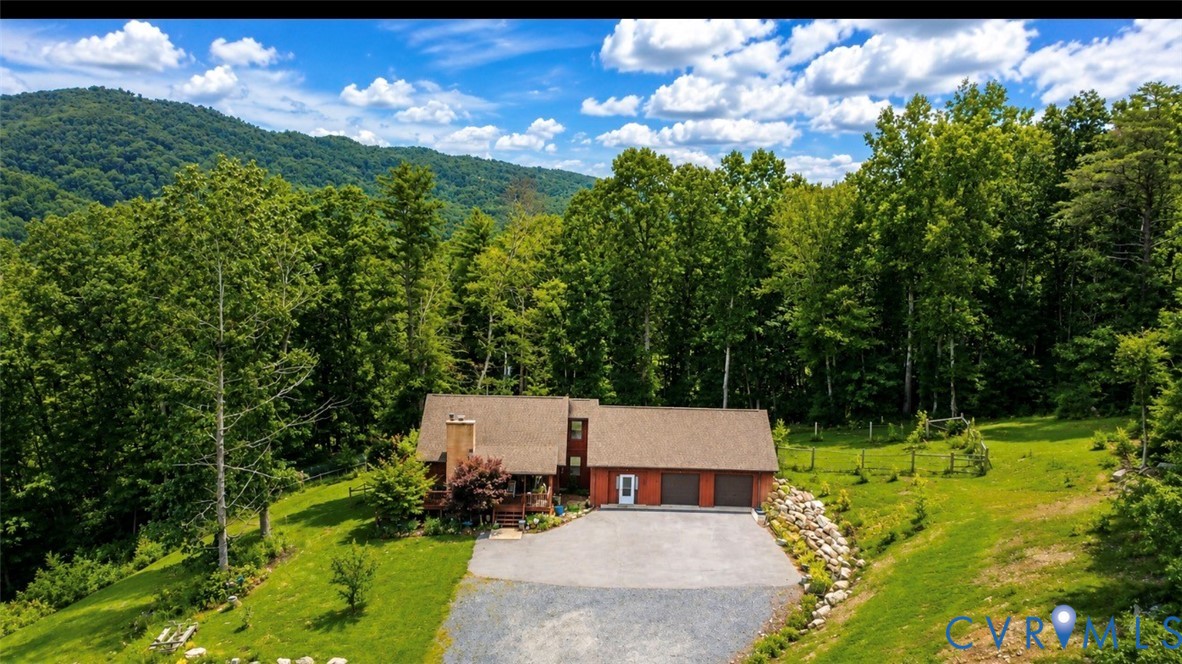 Multi-level residence featuring a stone chimney, attached three-car garage, gravel driveway, and mountain backdrop