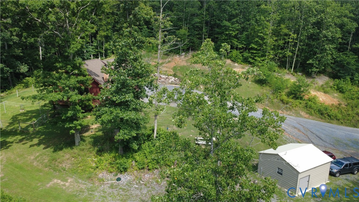 Wooded parcel featuring a gravel driveway, detached storage structure, and expansive grass acreage