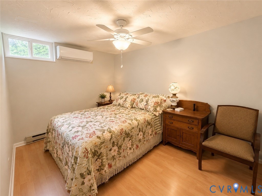 Wood-finish flooring, white ceiling fan with integrated lighting, and wall-mounted ductless climate control unit