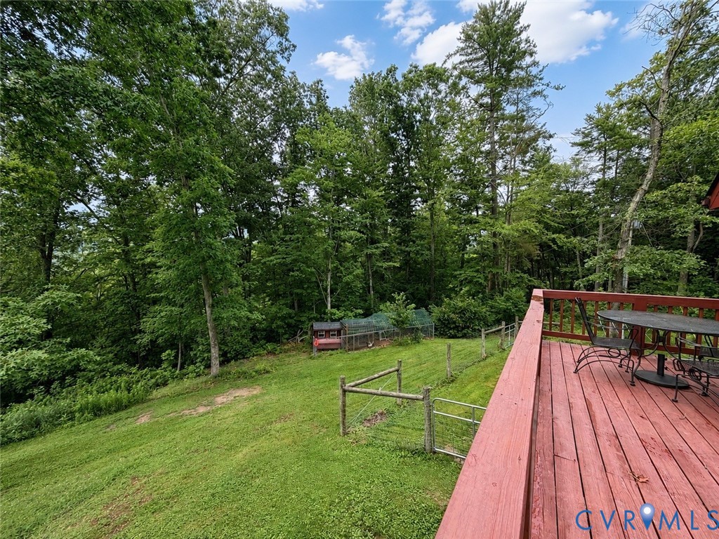 Elevated wooden deck with railing overlooking a sloped lawn and mature tree-lined perimeter