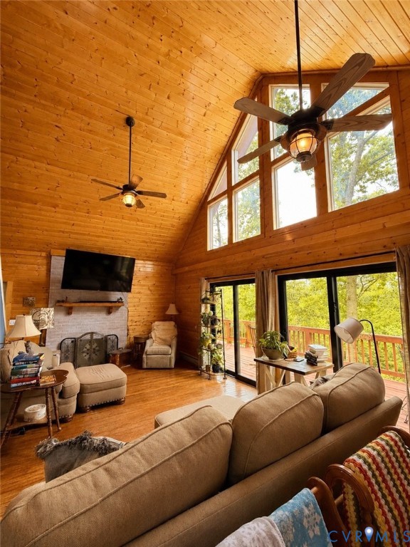 Vaulted ceilings with exposed wood paneling, floor-to-ceiling windows, stacked-stone fireplace, wood-finish flooring, and ceiling fans