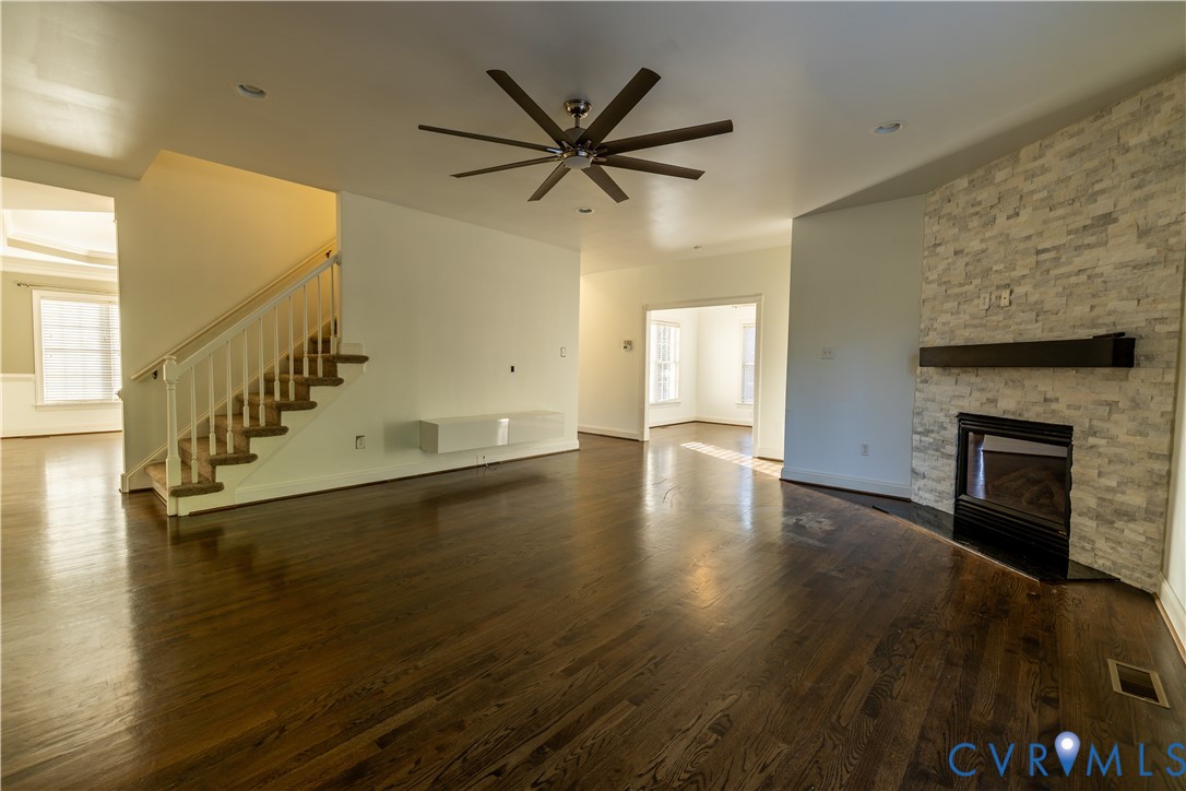 Interior featuring wood-finish flooring, a stone-veneer fireplace with a linear mantel, a wall-mounted floating console, recessed lighting, and a multi-blade ceiling fan