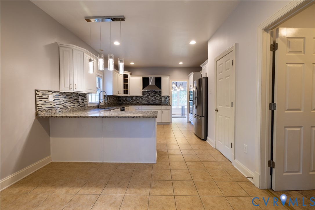 Kitchen featuring white cabinetry, stone countertops, multi-toned tile backsplash, stainless steel appliances, and multi-pendant lighting