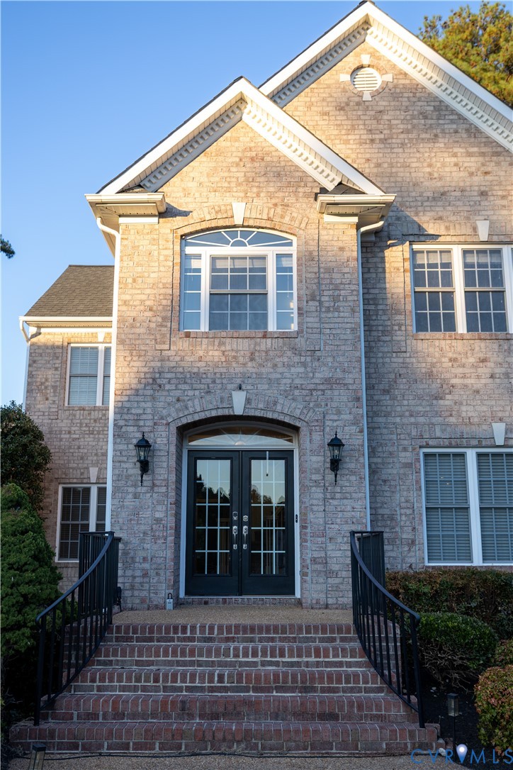 Brick exterior featuring a gabled roofline, a multi-pane arched transom window, double-entry doors, and a decorative brick staircase with black metal railings