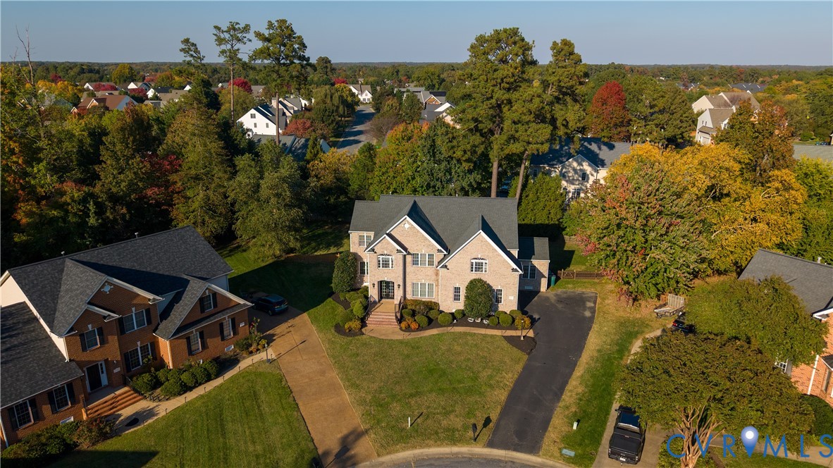 Two-story brick exterior featuring a multi-gabled roofline, asphalt shingle roofing, paved driveway, and mature landscaping