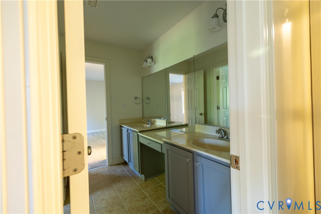 Dual-sink vanity with neutral-toned stone countertops, painted shaker-style cabinetry, tiled flooring, and oversized wall-mounted mirrors