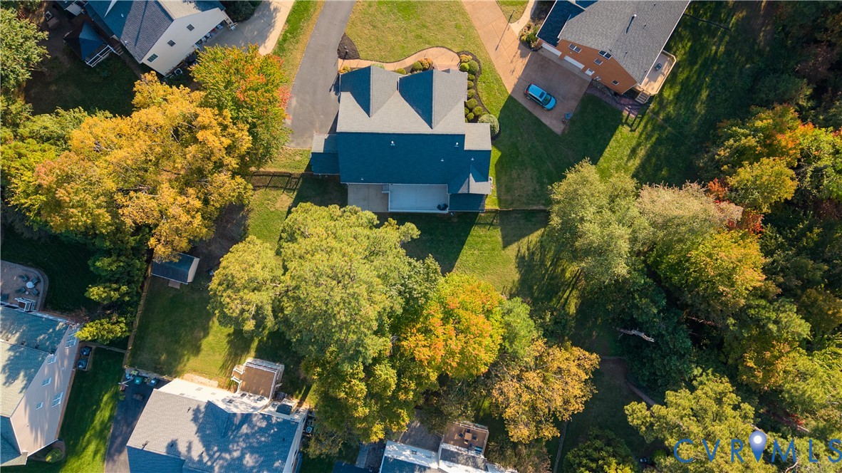 Aerial view featuring a multi-pitched roofline, expansive rear lawn, mature tree canopy, and a concrete patio