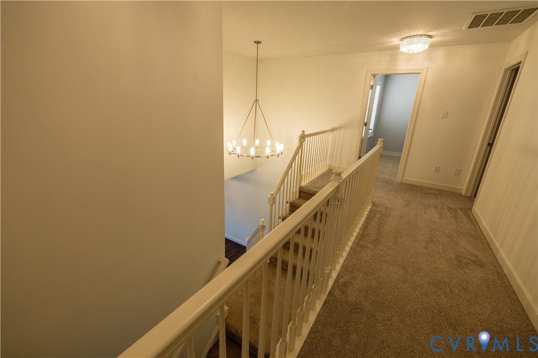 Upper landing featuring a tiered chandelier, carpeted flooring, and a staircase with a white painted railing