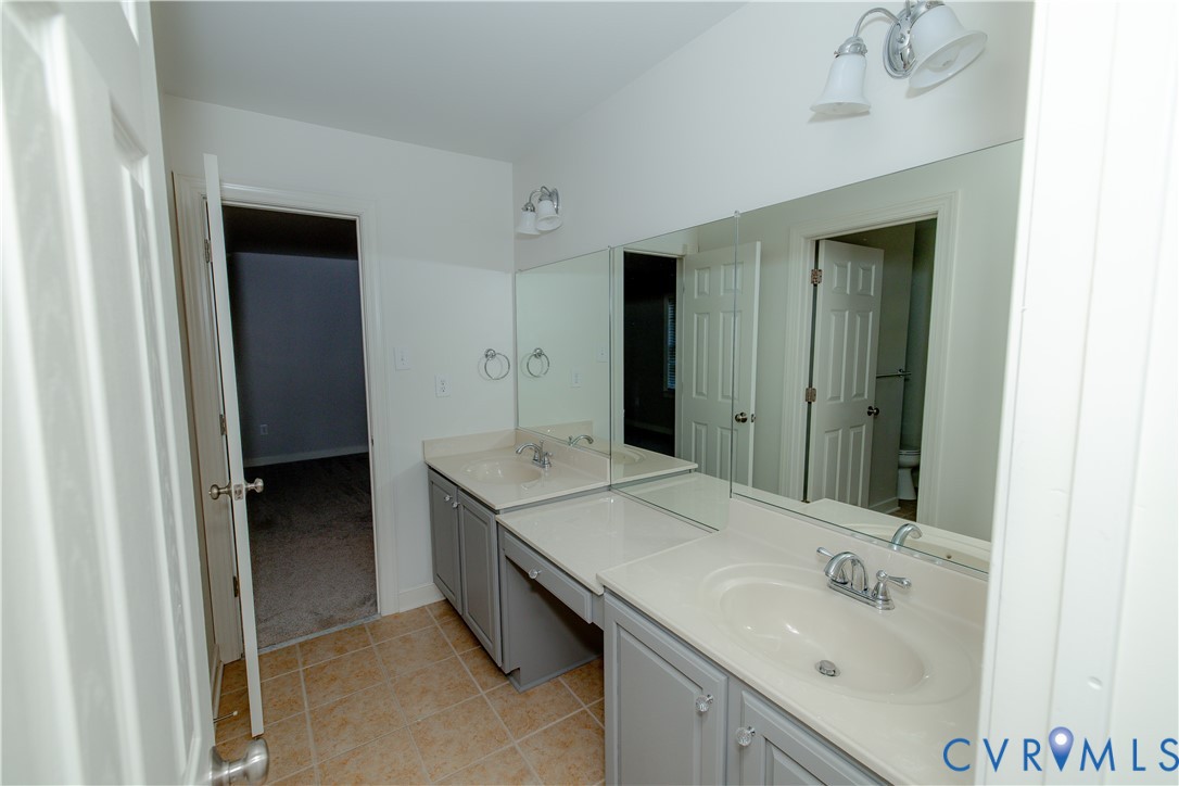 Dual-sink vanity featuring neutral-toned cabinetry, integrated basins, solid surface countertops, polished chrome fixtures, and a large wall-mounted mirror