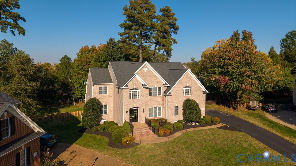 Brick exterior residence featuring a multi-gabled roofline, front entryway with brick steps, paved driveway, and mature landscaping