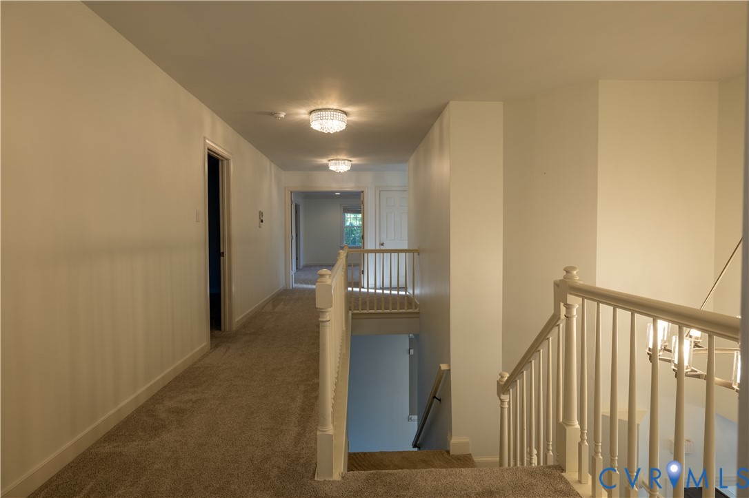 Hallway featuring wall-to-wall carpeting, white interior doors, decorative flush-mount ceiling lighting, and a white baluster railing