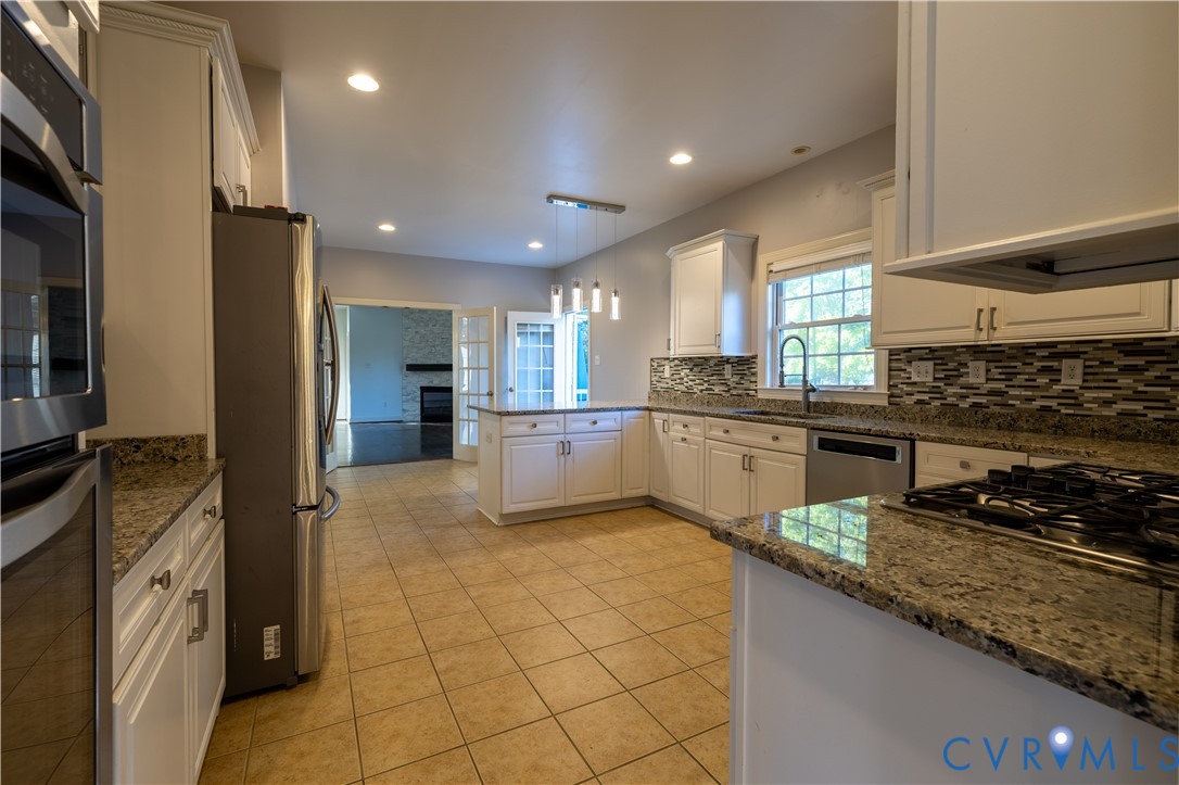 Kitchen featuring white cabinetry, stone countertops, stainless steel appliances, tiled backsplash, and tile flooring