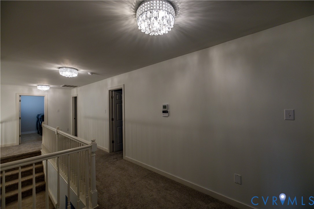 Hallway featuring multiple crystal-accented semi-flush mount light fixtures, carpeted flooring, and a wooden banister railing