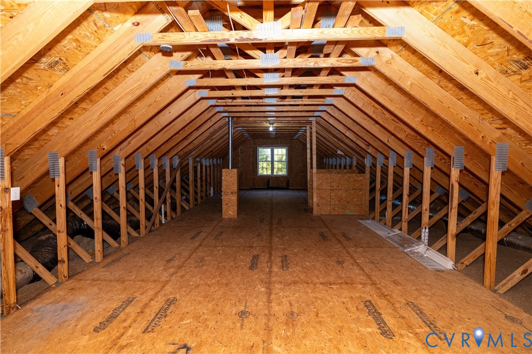 Unfinished attic space featuring exposed wood-truss construction, plywood subflooring, and a single pane window
