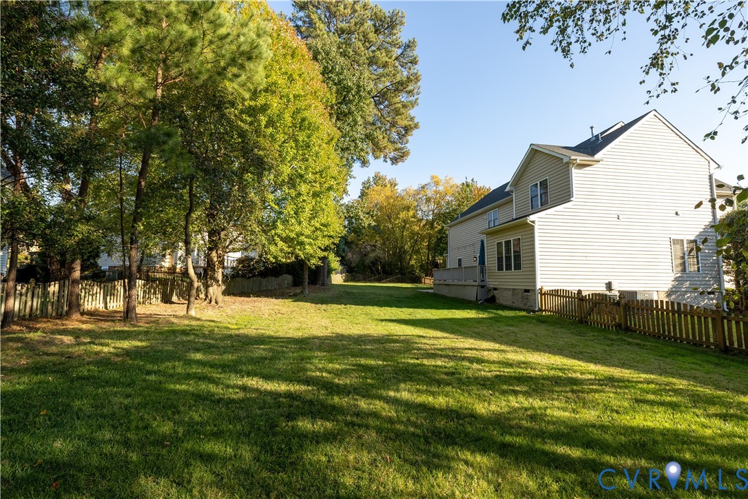 Expansive backyard featuring a spacious lawn, perimeter wood fencing, and mature trees